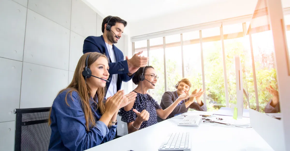 Diverse Colombian tech support team celebrating success in a bright office space.